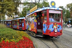 Bunter Ebbelwei-Express auf Gleisen fährt durch blumengeschmückte Straße