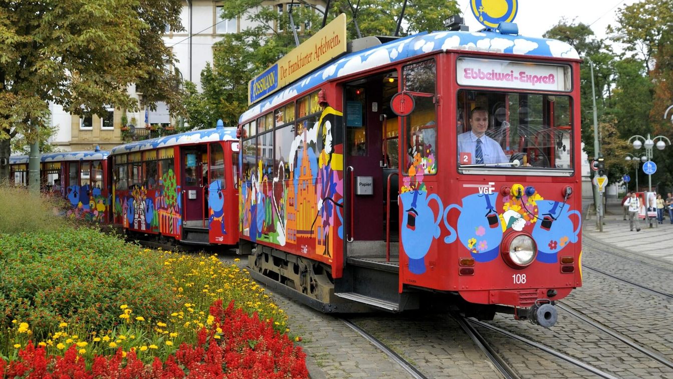 Bunter Ebbelwei-Express auf Gleisen fährt durch blumengeschmückte Straße