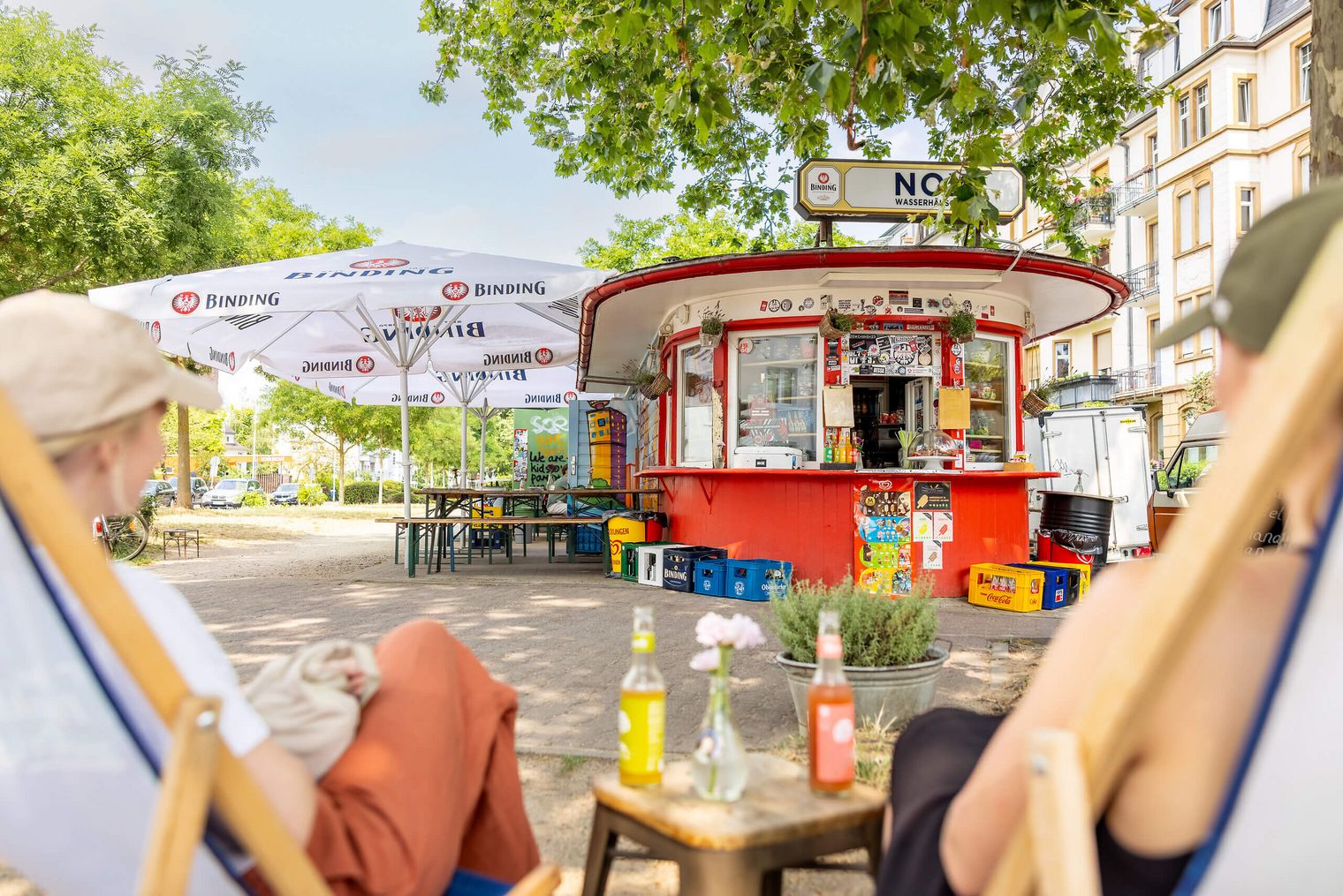 Rotes Wasserhäuschen mit Außenbereich, Sonnenschirmen und Menschen.