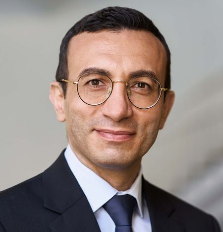 Mann mit Brille im Anzug vor hellem Hintergrund.