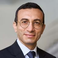 Mann mit Brille im Anzug vor hellem Hintergrund.