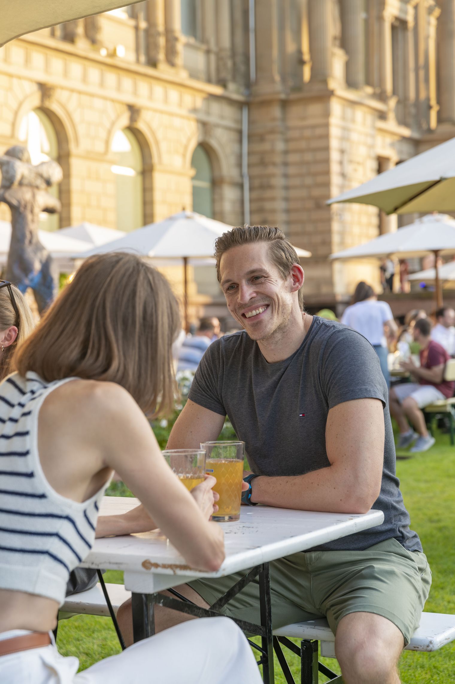 Paar sitzt mit Getränken im Garten vor historischem Gebäude